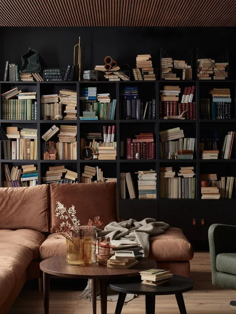 Salon z czekoladową sofą, czarną biblioteczką pełną książek i dekoracyjnym sufitem z lameli